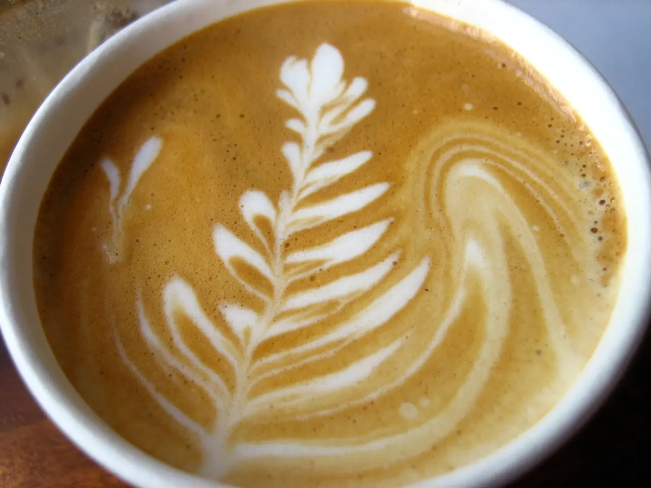 In this picture I can see there is a coffee mug and there is some coffee in it with a design.