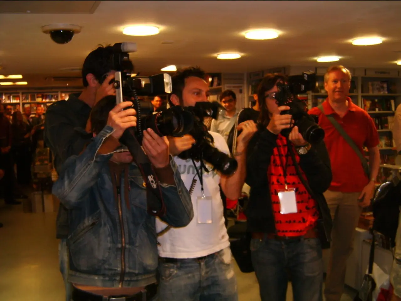 People are standing in a room wearing id cards and holding cameras. There are books in the book...