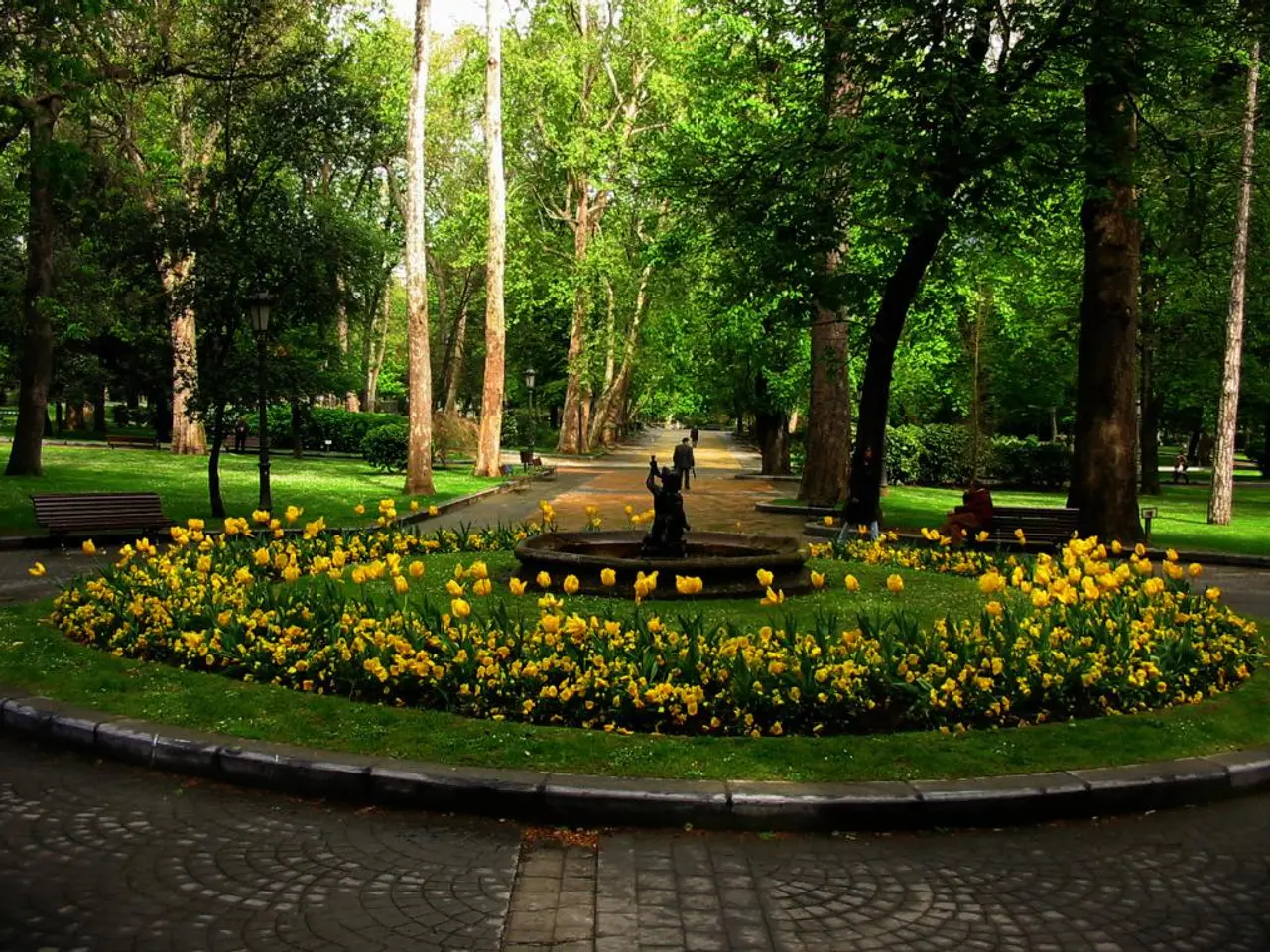 In this picture there is a small fountain in the middle of the garden and some yellow color...