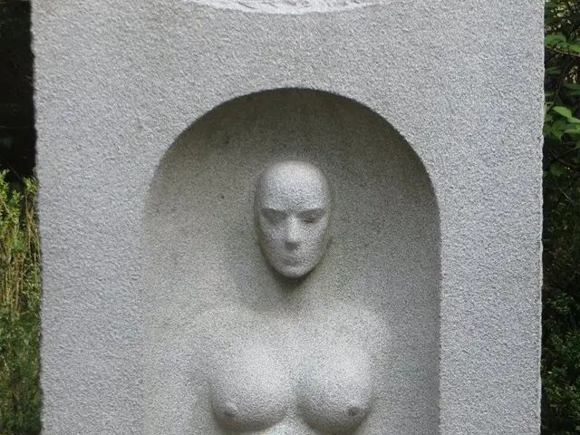 In this image there is a stone having a sculpture. Stone is on the floor. Background there are few...