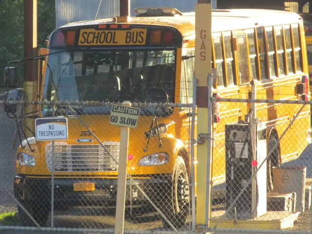 In this picture there are buses on the road. In the foreground there is a fence and there are poles...